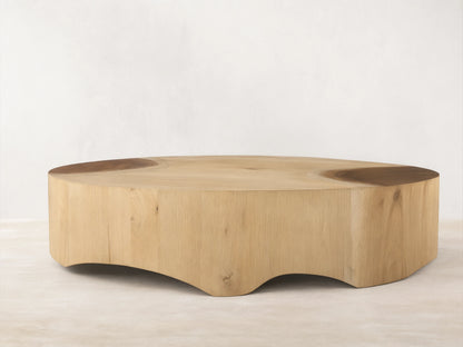 Front view of a light wood coffee table, round with a solid, inwardly curved base, showcasing subtle top surface details.