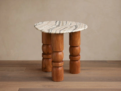 Rune End Table with a round, marbled stone top and unique carved wooden legs, set on a wooden floor against a beige wall.