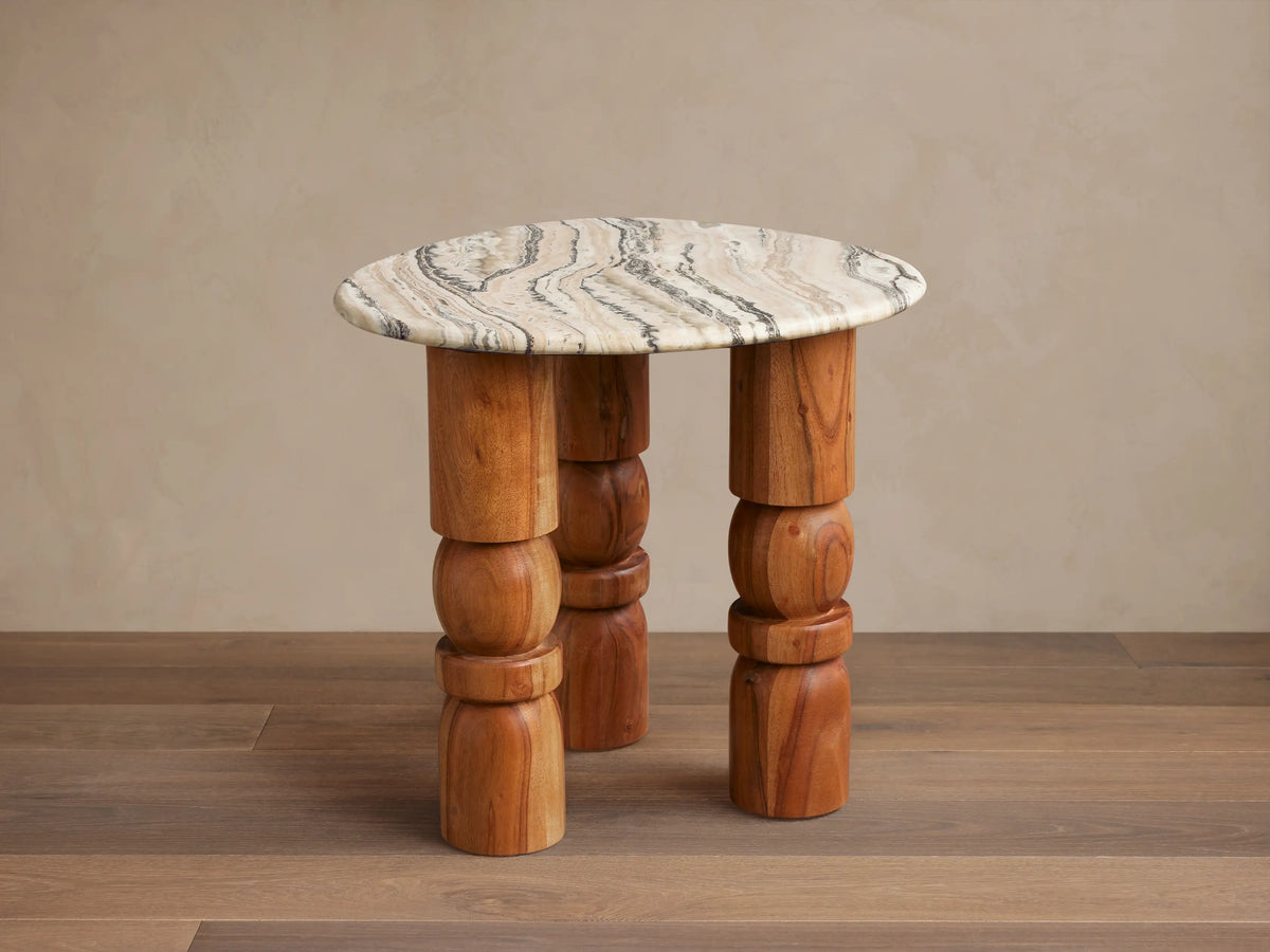 Rune End Table with a round, marbled stone top and unique carved wooden legs, set on a wooden floor against a beige wall.