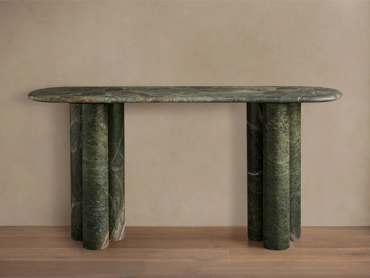 Serafin Console Table, oval green marble top, three rounded column legs on each side, against a neutral wall & wood floor.