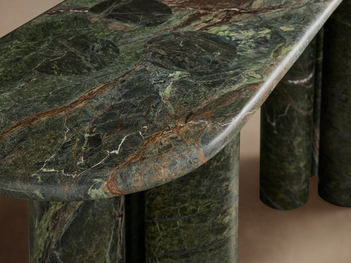 Serafin Console Table: Oval dark green marble with natural veining, supported by four thick cylindrical legs, against a plain wall.