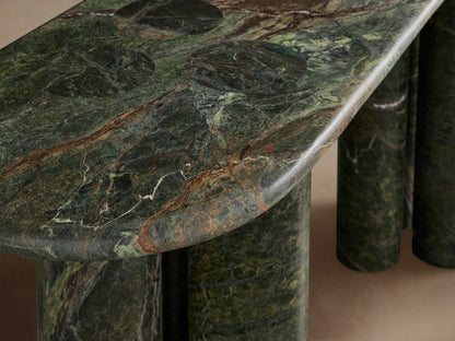 Serafin Console Table: Oval dark green marble with natural veining, supported by four thick cylindrical legs, against a plain wall.