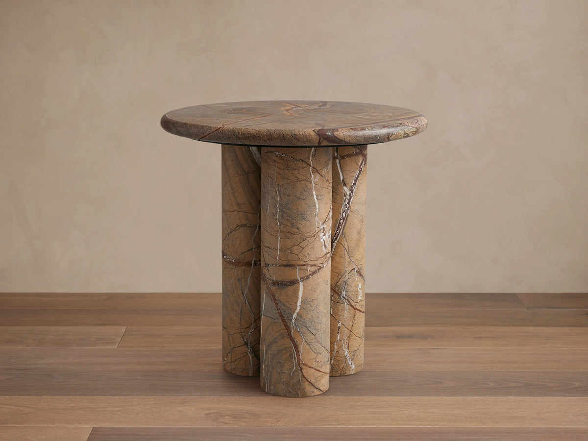 Serafin End Table with a round stone top and three cylindrical legs. Natural veining in shades of brown, highlighting a modern design.