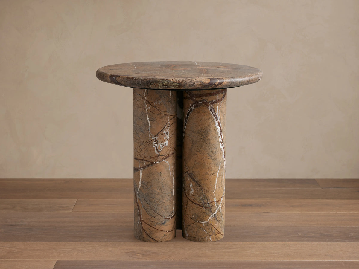 Serafin End Table with a round stone top and three cylindrical legs. Natural veining in shades of brown, highlighting a modern design.