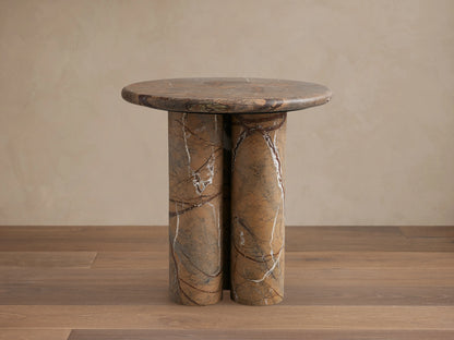 Serafin End Table with a round stone top and three cylindrical legs. Natural veining in shades of brown, highlighting a modern design.
