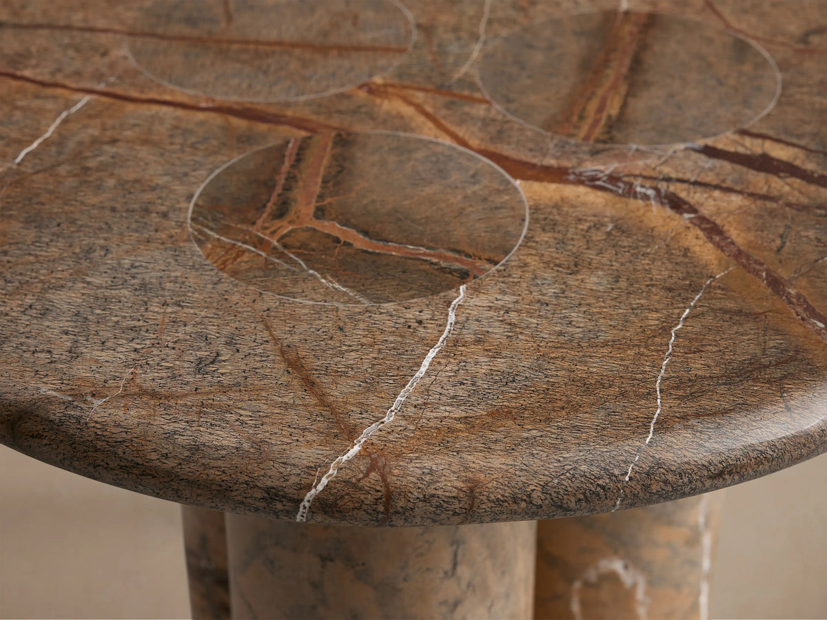 Front view of the brown marble Round Pedestal Table, featuring white and dark veins, and three thick cylindrical legs.