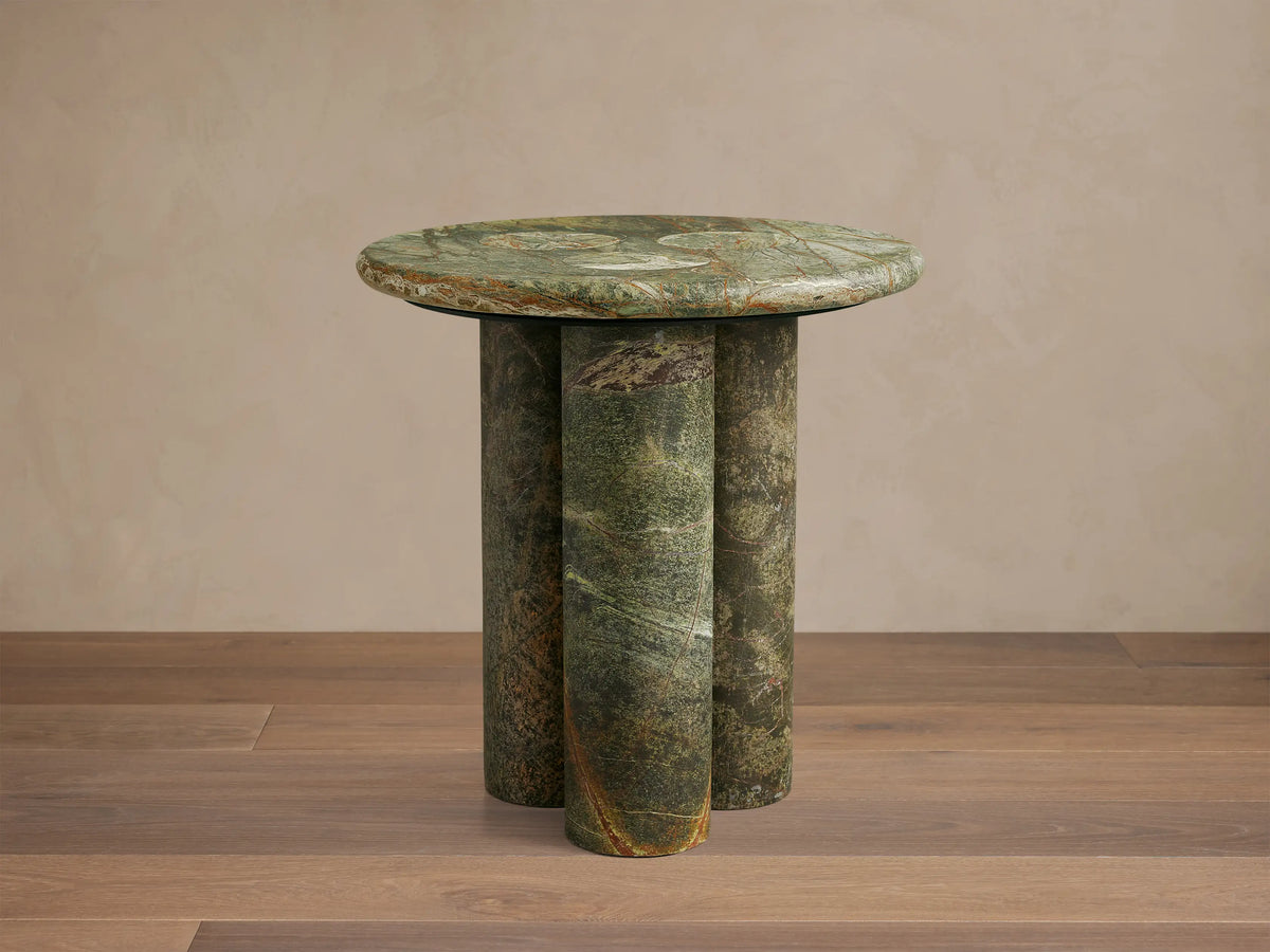 Front view of a round green marble side table with three cylindrical legs, showing natural brown and white veining.