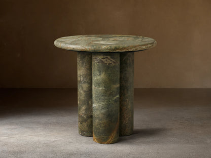 Front view of a round green marble side table with three cylindrical legs, showing natural brown and white veining.