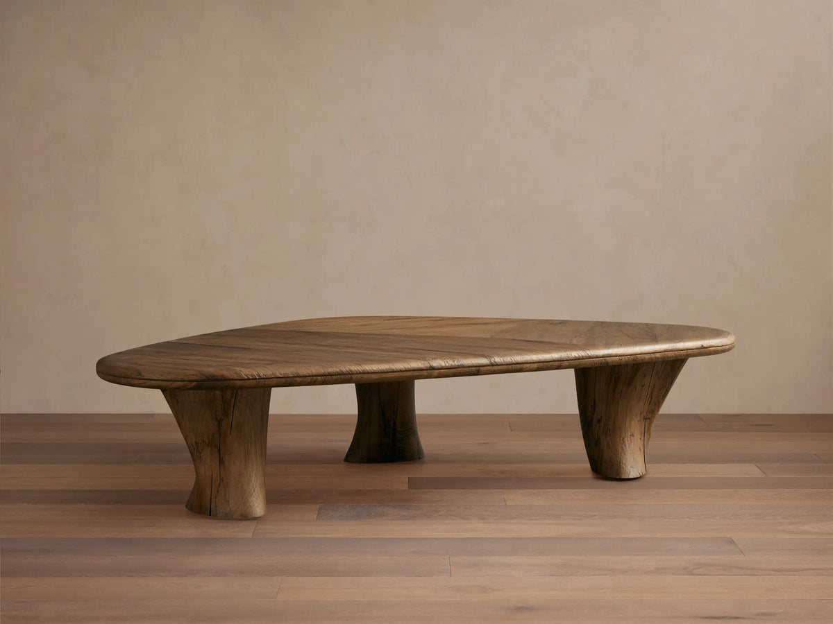 Soumaya Coffee Table: Organic, triangular spalted primavera wood coffee table with radial grain top, thick mahogany legs on wood floor.
