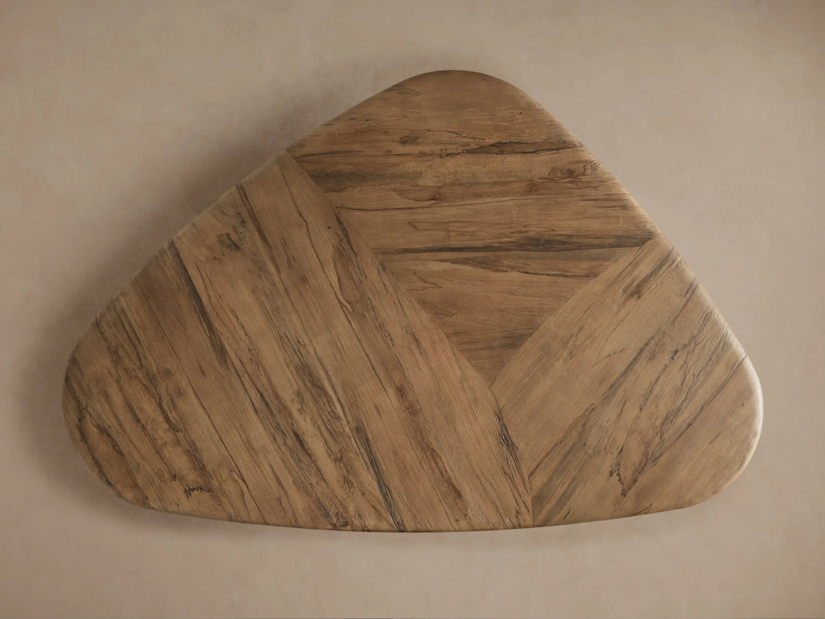 Angled close-up of Soumaya Coffee Table, showing light brown spalted primavera wood top with radial pattern & thick, curved mahogany leg.