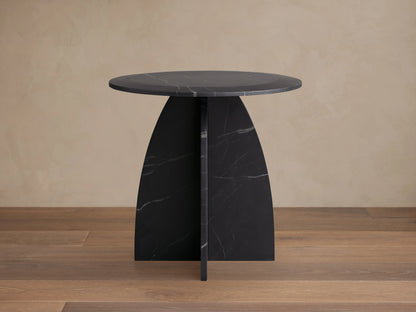 Round Solstice End Table made of Black Marquina marble with a smooth surface, curved legs, and wooden floor background.