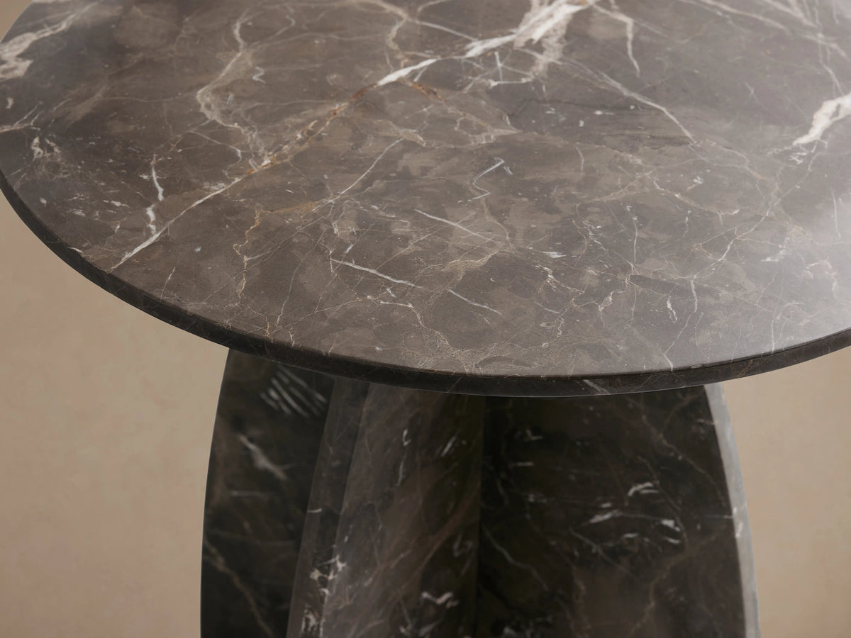 A round Solstice End Table with a dark marble top and curved marble laminate legs. The surface shows natural veining patterns.