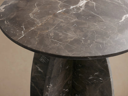 A round Solstice End Table with a dark marble top and curved marble laminate legs. The surface shows natural veining patterns.