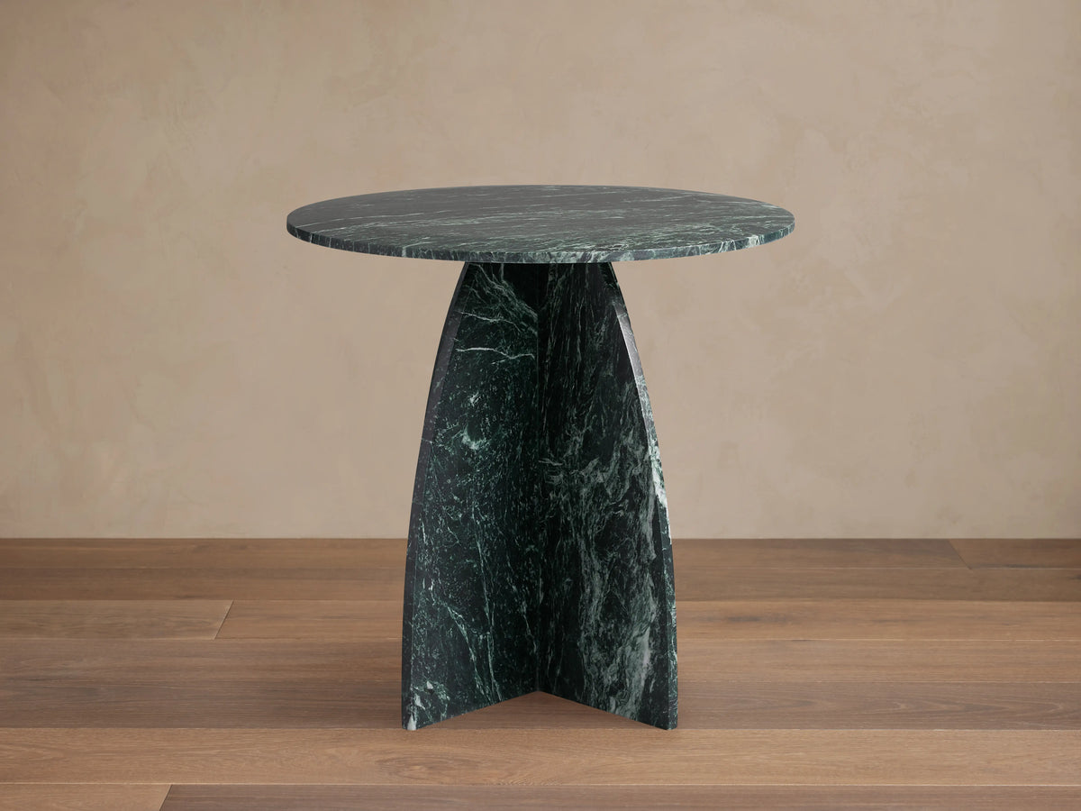 Solstice End Table in green marble with a round top, featuring sleek, sculpted laminate legs on a wooden floor.