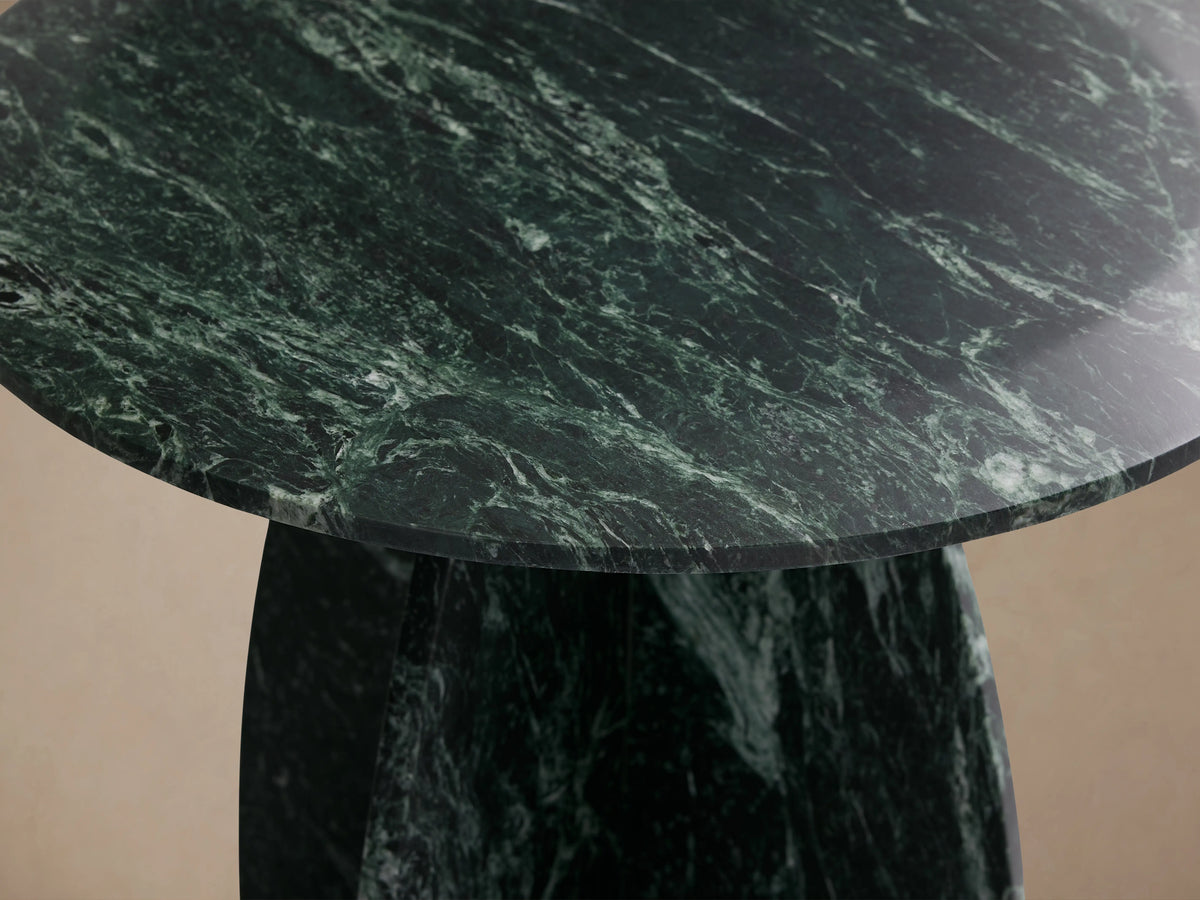 Solstice End Table in green marble with a round top, featuring sleek, sculpted laminate legs on a wooden floor.