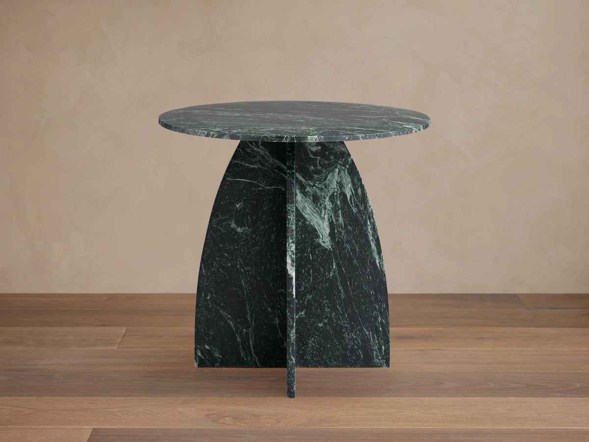 Solstice End Table with round green marble top and matching curved table legs, showcasing unique veining patterns.