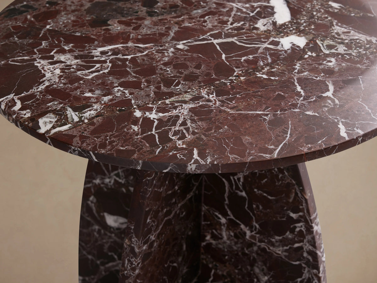Solstice End Table with a round top and unique curved pedestal base. Made from deep red marble with white veining.