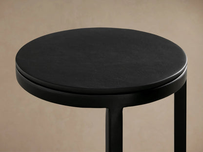 Soma Martini Table with a sleek black metal frame, round top, and circular base, standing on a wooden floor against a beige wall.