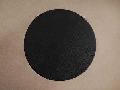 A round, dark black Soma Martini Table with a sleek, minimalist design. The table's top is smooth, and it rests on slender legs.