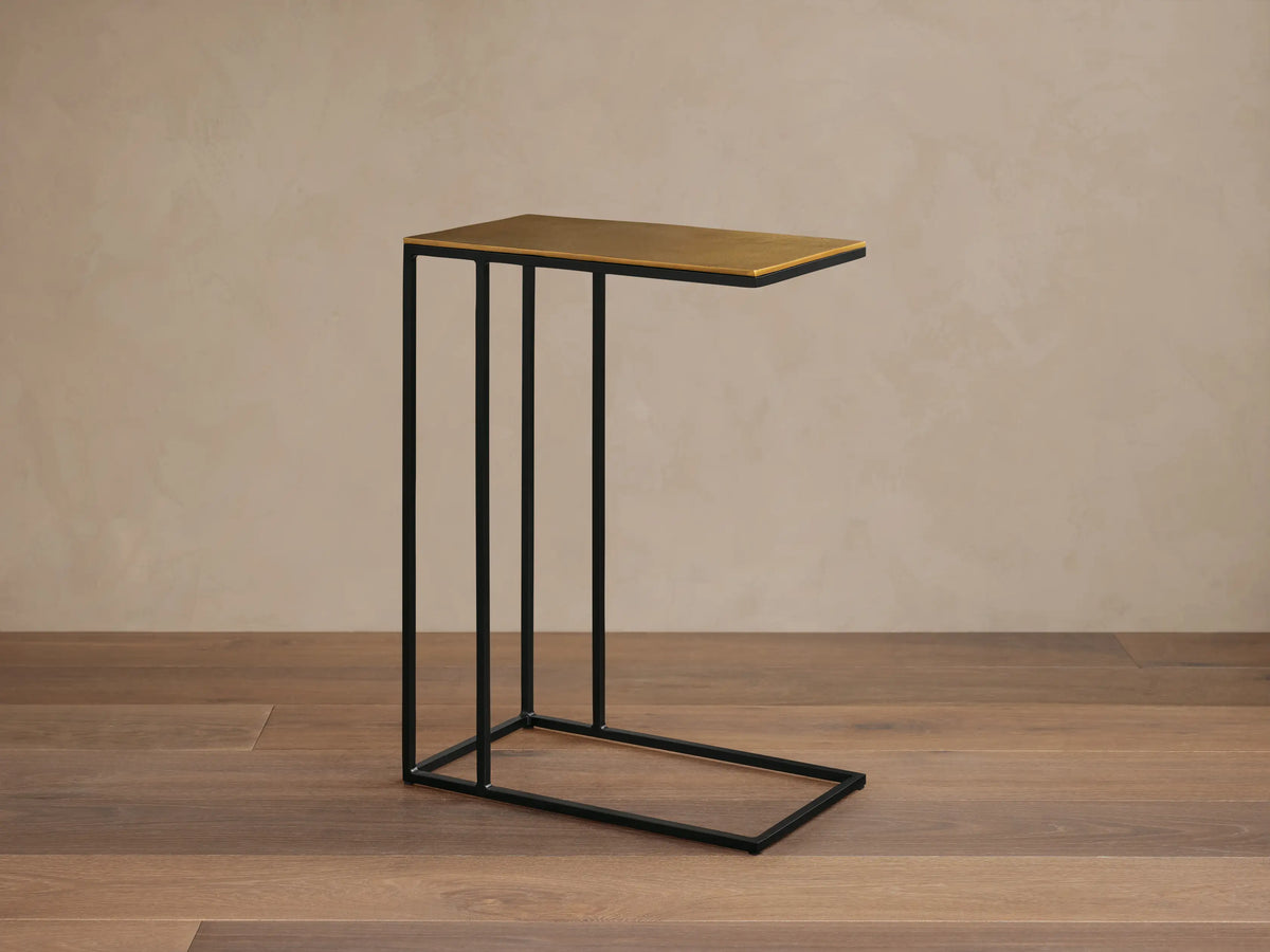 Front view of the Soma C Table, with a rectangular patinaed gold aluminum top and a black C-shaped stainless steel frame.