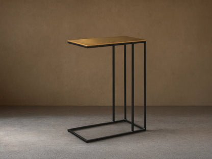 Front view of the Soma C Table, with a rectangular patinaed gold aluminum top and a black C-shaped stainless steel frame.
