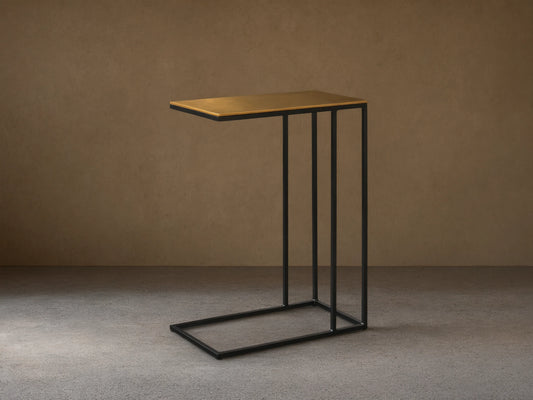 Front view of the Soma C Table, with a rectangular patinaed gold aluminum top and a black C-shaped stainless steel frame.