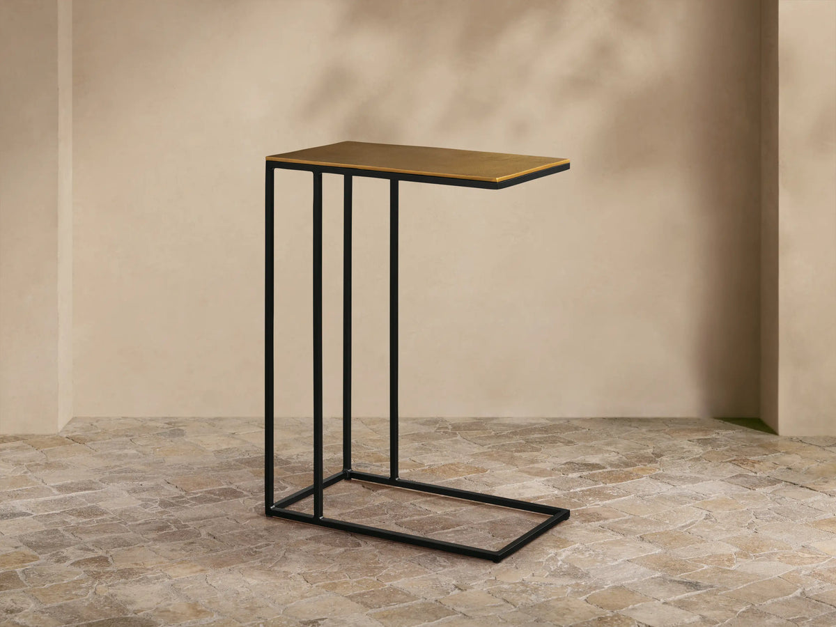 Front-left view of the Soma C Table, featuring a gold rectangular top and a black C-shaped metal base.