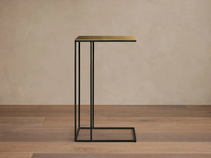 Front view of the Soma C Table, featuring a black C-shaped metal base and a rectangular gold-toned top.