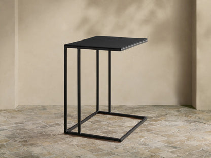 Matte black Soma Wide C Table with square aluminum top and stainless steel C-frame, on a textured stone floor.