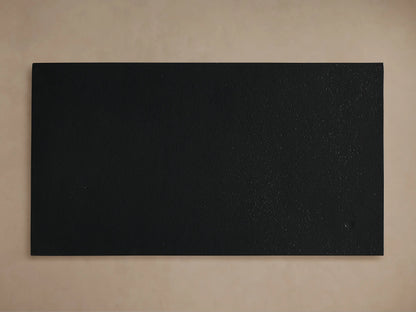 Close-up of Soma C Table's matte black tabletop with dark frame & legs, angled against a light beige background.