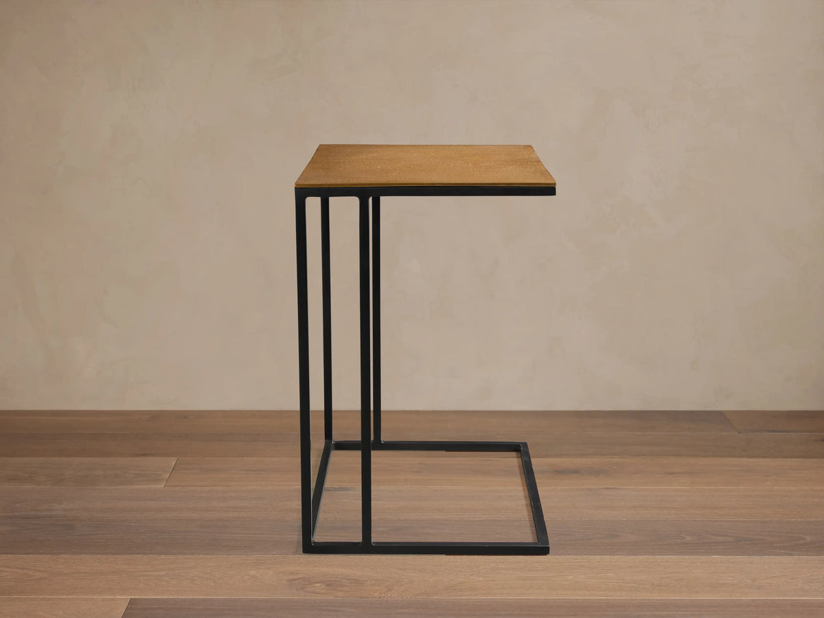 Soma Wide C Table with light brown wooden top and black metal C-frame, on a stone floor against a beige wall.