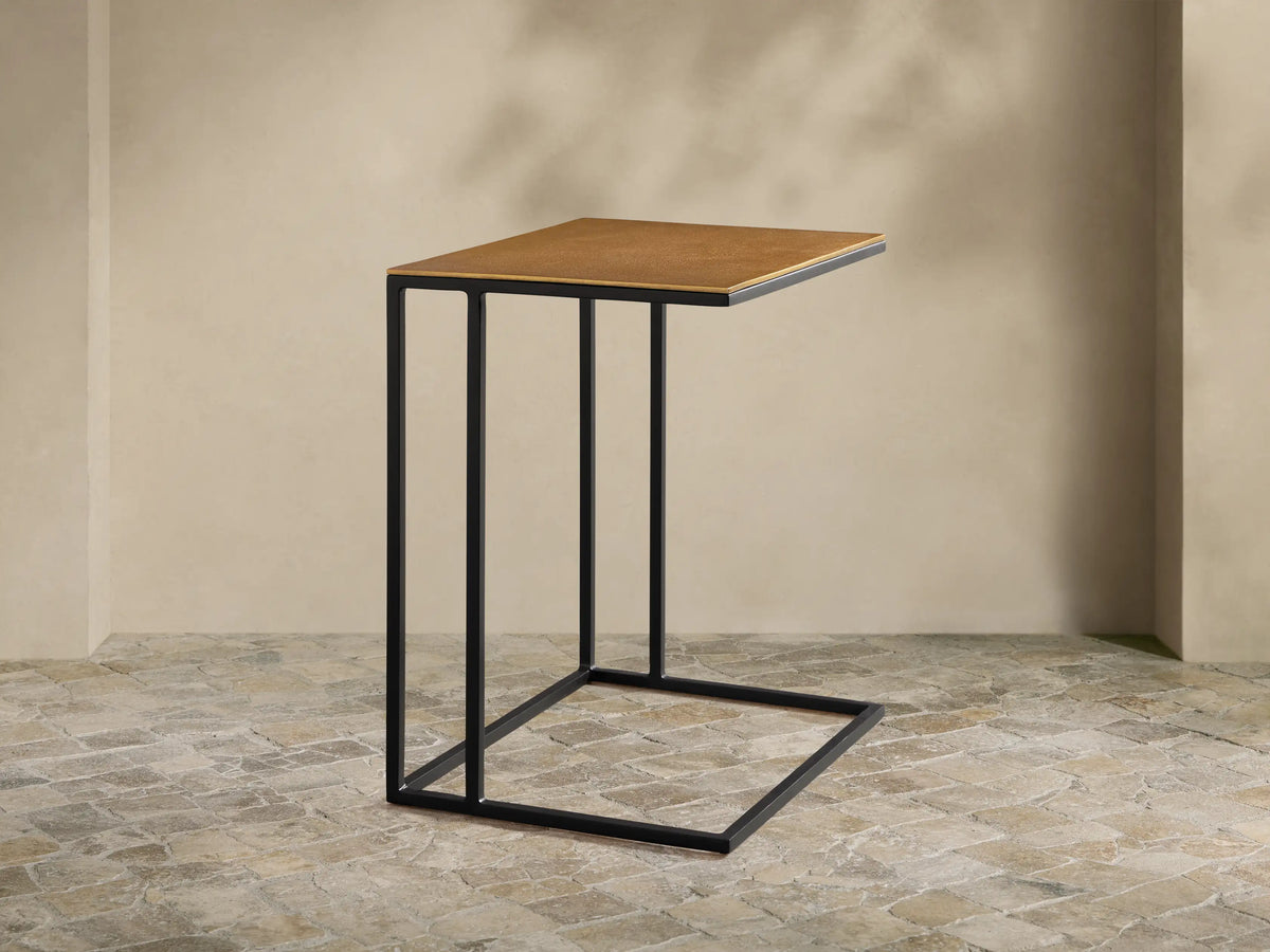 Soma Wide C Table with a rectangular, golden-brown patinaed aluminum top and a black stainless steel C-frame on a wood floor.