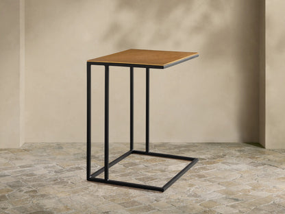 Soma Wide C Table with a rectangular, golden-brown patinaed aluminum top and a black stainless steel C-frame on a wood floor.