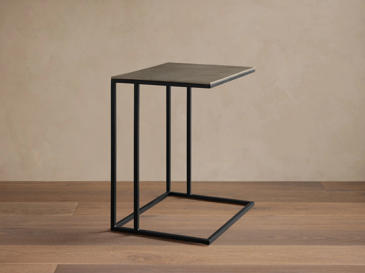 Soma Wide C Table, dark grey rectangular top with patina finish, on a black C-shaped base. Viewed against a light wall.
