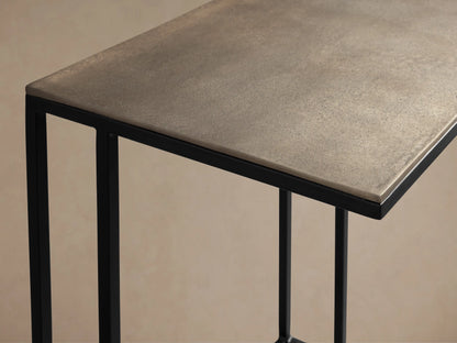 Soma Wide C Table with rectangular gray patinaed aluminum top and black C-shaped metal base, on a wooden floor.