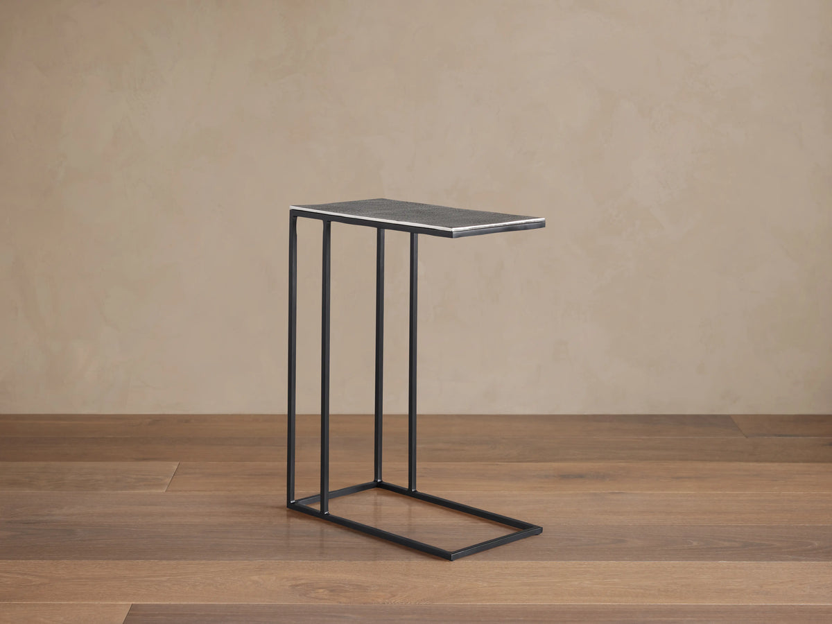 Soma C Table with a rectangular aluminum tabletop, dark patinaed finish, and thin iron base, on a wooden floor.