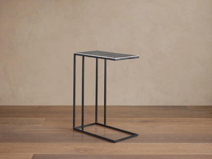 Soma C Table with a rectangular aluminum tabletop, dark patinaed finish, and thin iron base, on a wooden floor.