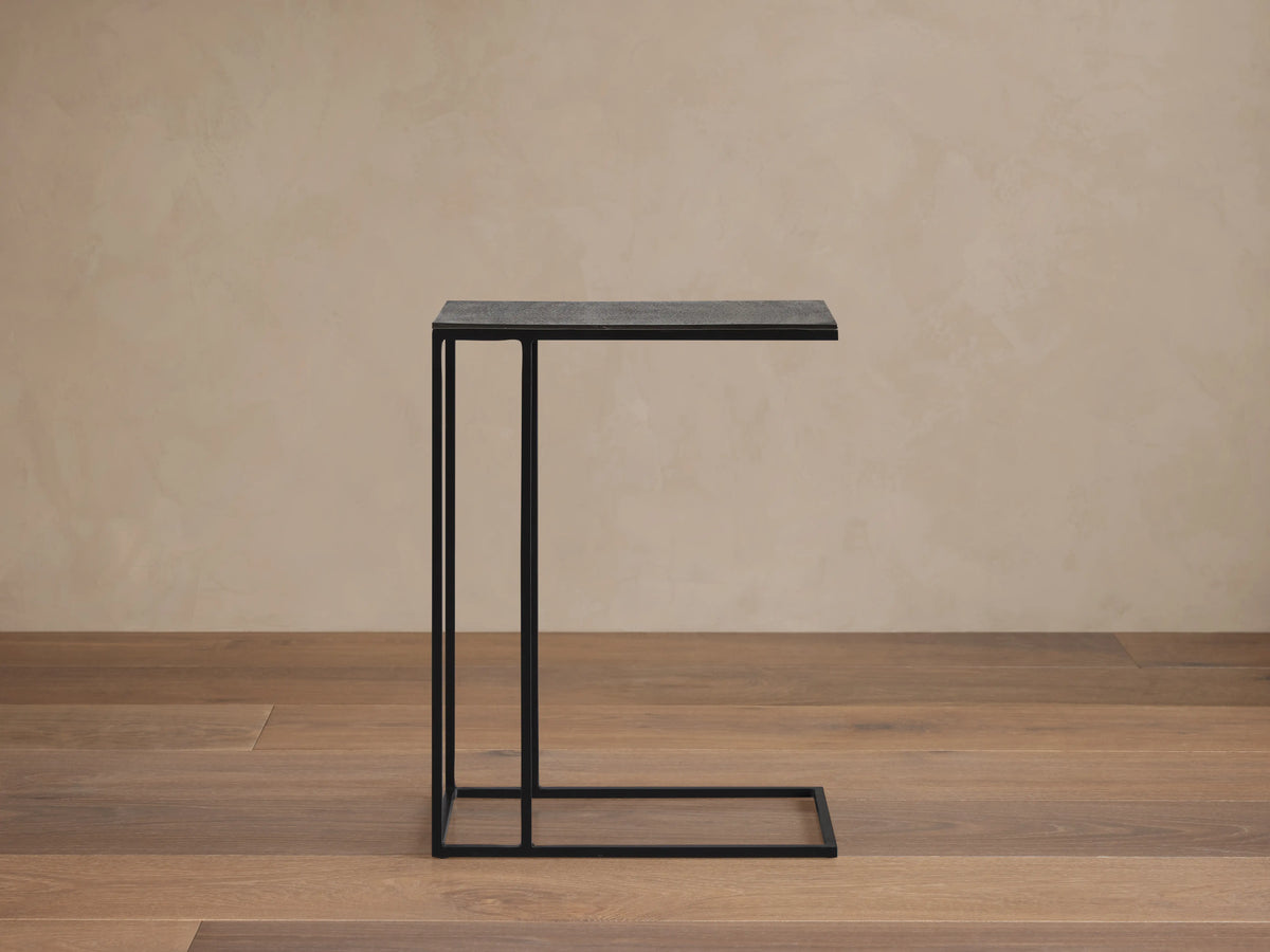Soma C Table with a rectangular aluminum tabletop, dark patinaed finish, and thin iron base, on a wooden floor.