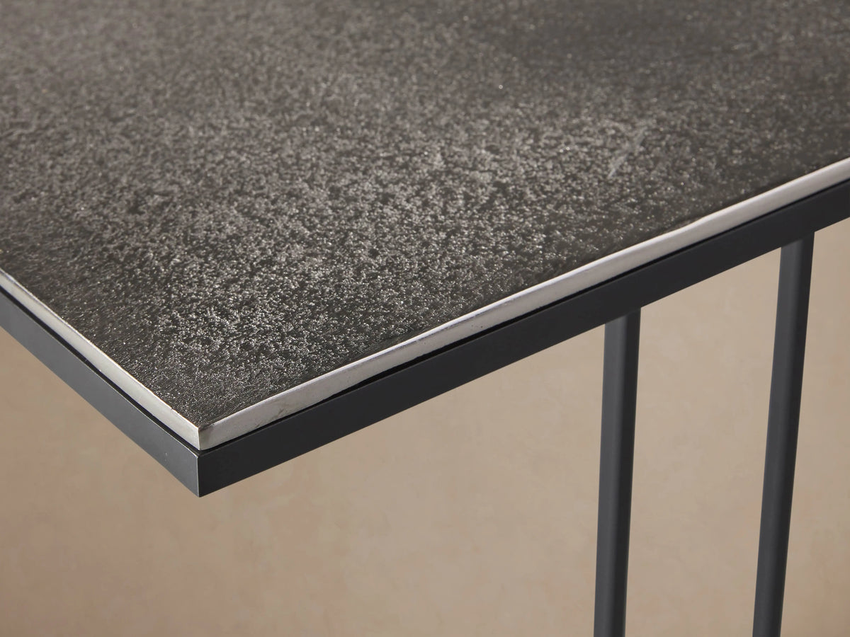 Soma C Table with a black cast aluminum top and solid iron base in C shape, set on wooden floor against a beige wall.
