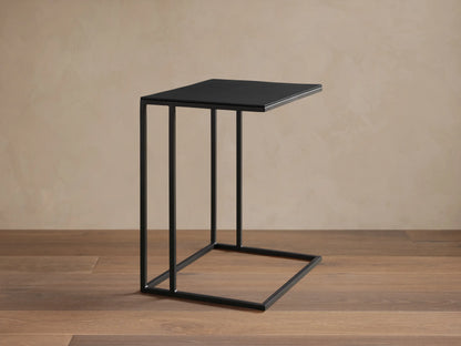 Black Soma C Table with square top and slender C-shaped metal frame on a wooden floor against a light wall.
