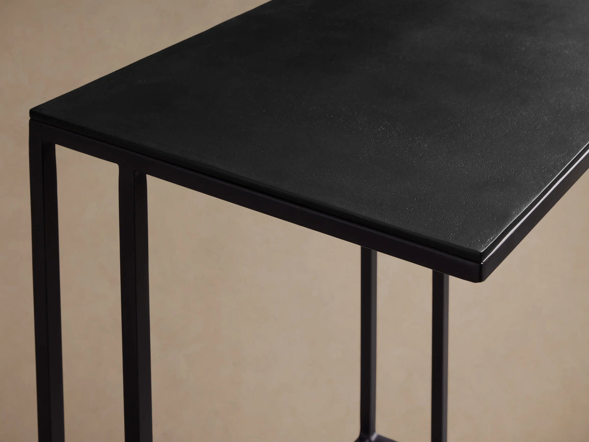 Soma C Table, close-up. Textured black rectangular top and dark frame, angled against a light tan background.