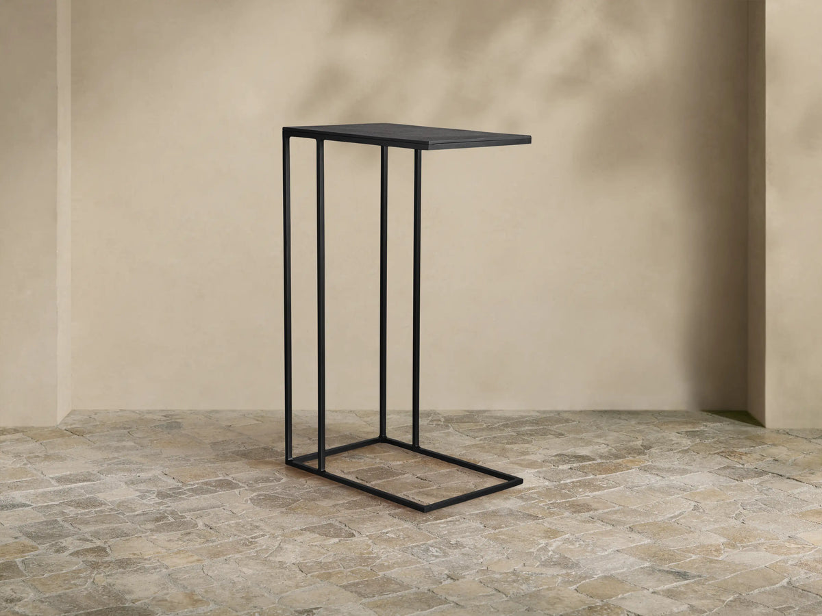 Black Soma C Table, featuring a rectangular top and sleek C-shaped base, standing on a textured tiled floor in a neutral room.