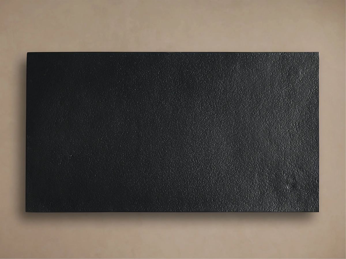 Close-up of Soma C Table's textured, dark grey tabletop with hand-applied patina and smooth black metal frame.