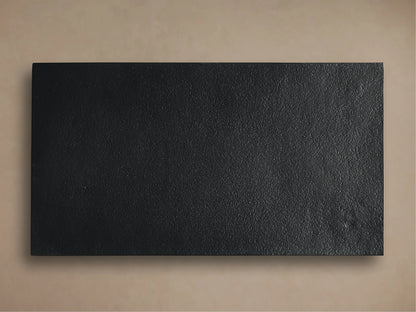 Close-up of Soma C Table's textured, dark grey tabletop with hand-applied patina and smooth black metal frame.