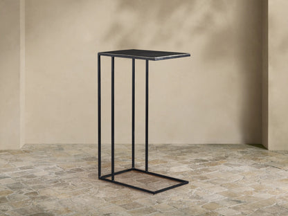 Black Soma C Table with a rectangular dark tabletop and thin metal C-frame, on a light stone floor against a beige wall.