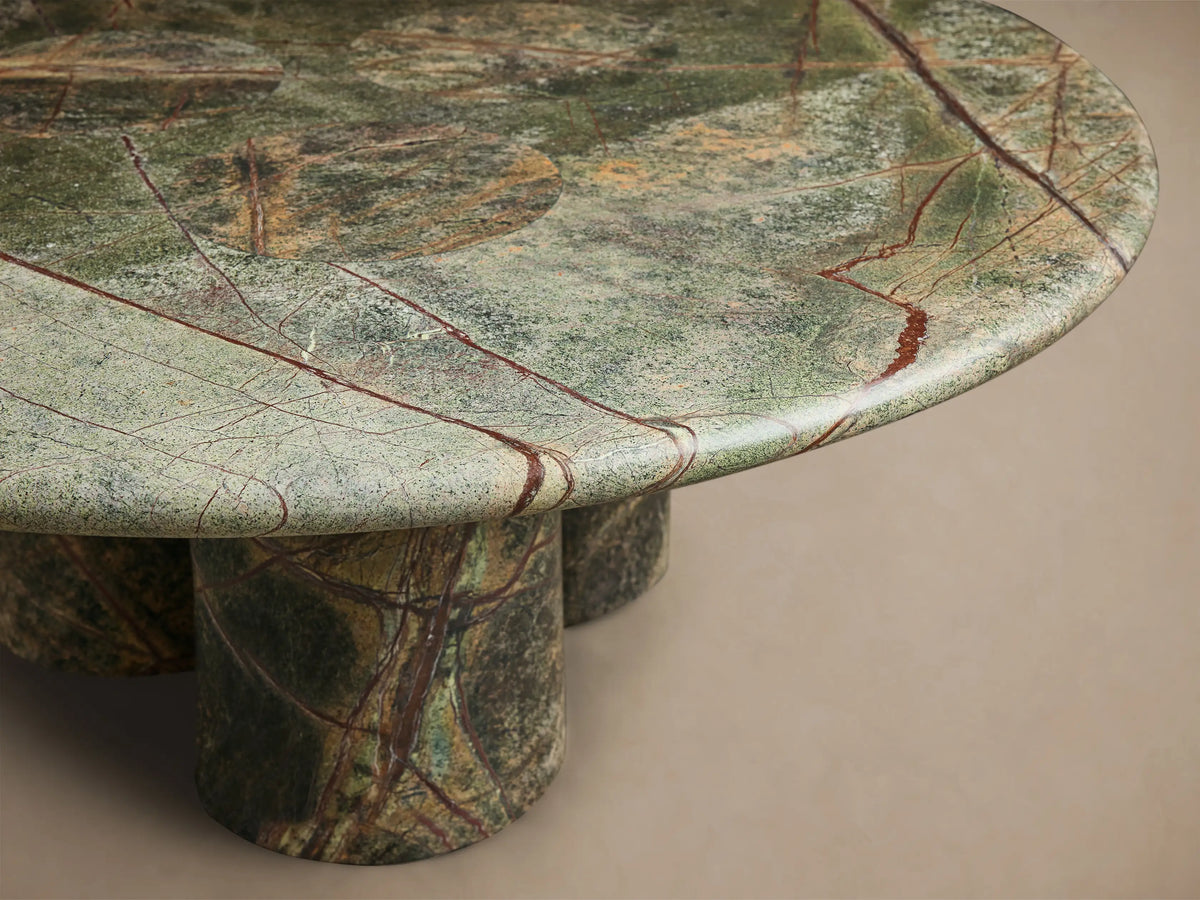 Close-up of the round green marble Serafin Coffee Table, featuring brown and red veins and three thick cylindrical legs.