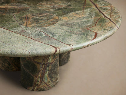 Close-up of the round green marble Serafin Coffee Table, featuring brown and red veins and three thick cylindrical legs.