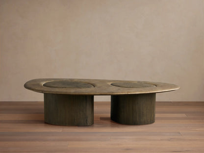 Sucurro Coffee Table: Elongated oxidized aluminum top with two dark circular depressions, supported by two thick dark wood bases.