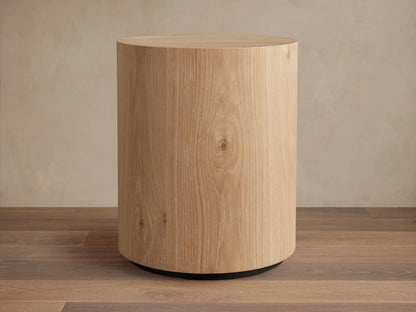 Sullivan Round End Table made of solid oak with a natural grain finish, cylindrical shape, on a black plinth-style base.