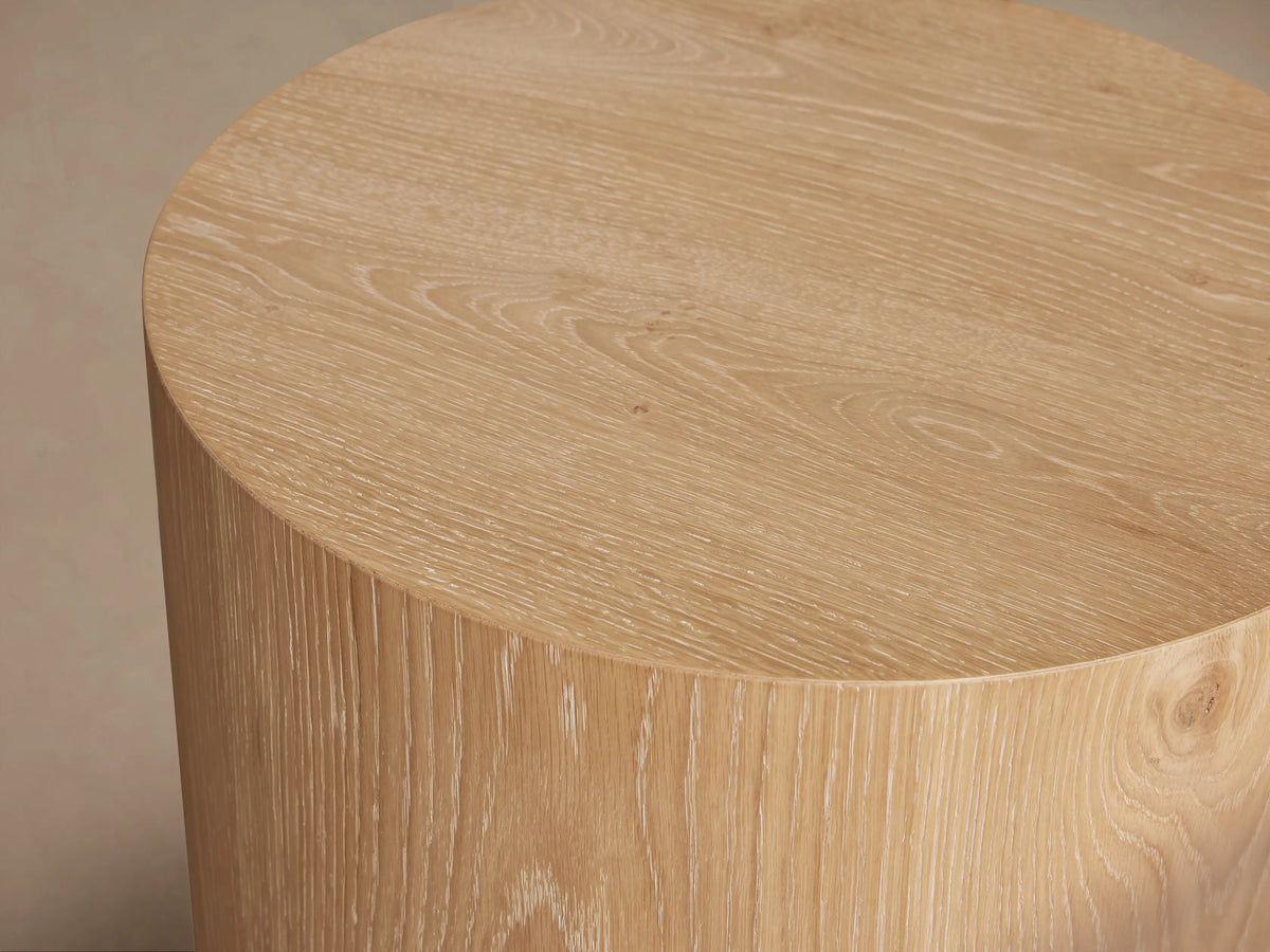 Sullivan Round End Table made of solid oak with a natural grain finish, cylindrical shape, on a black plinth-style base.
